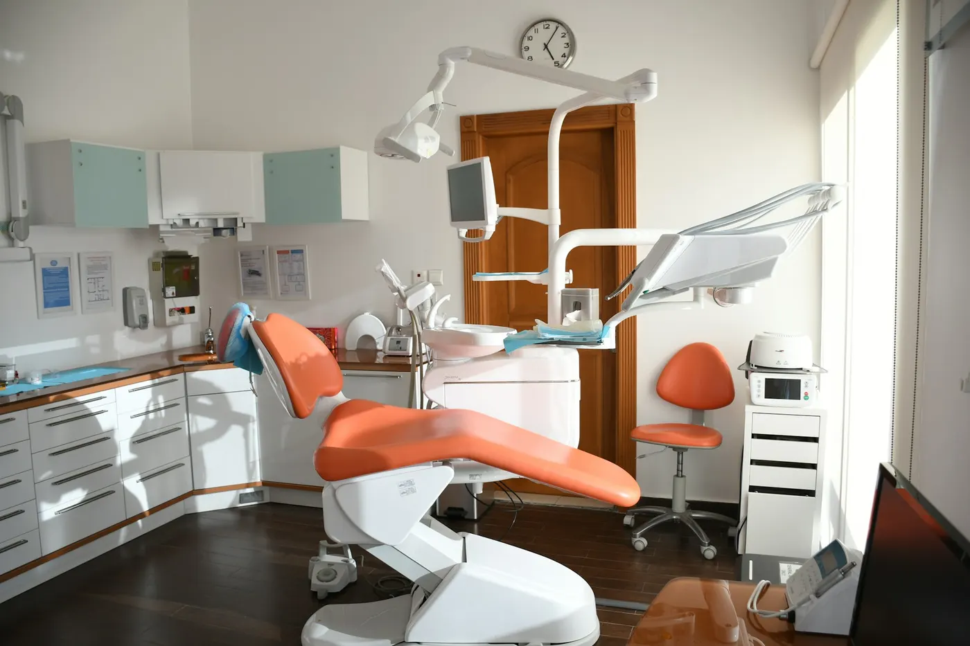 An empty dental surgery with an orange patient chair, overhead light and white cabinets
