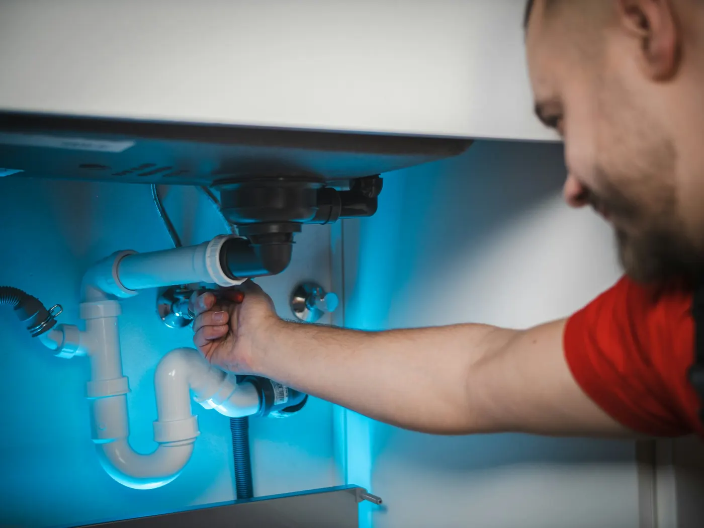 A plumber reaching under a sink to tighten a fitting on the waste pipe