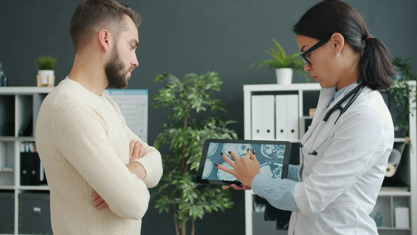 A clinician in a white coat showing a patient a scan on a tablet in a consulting room